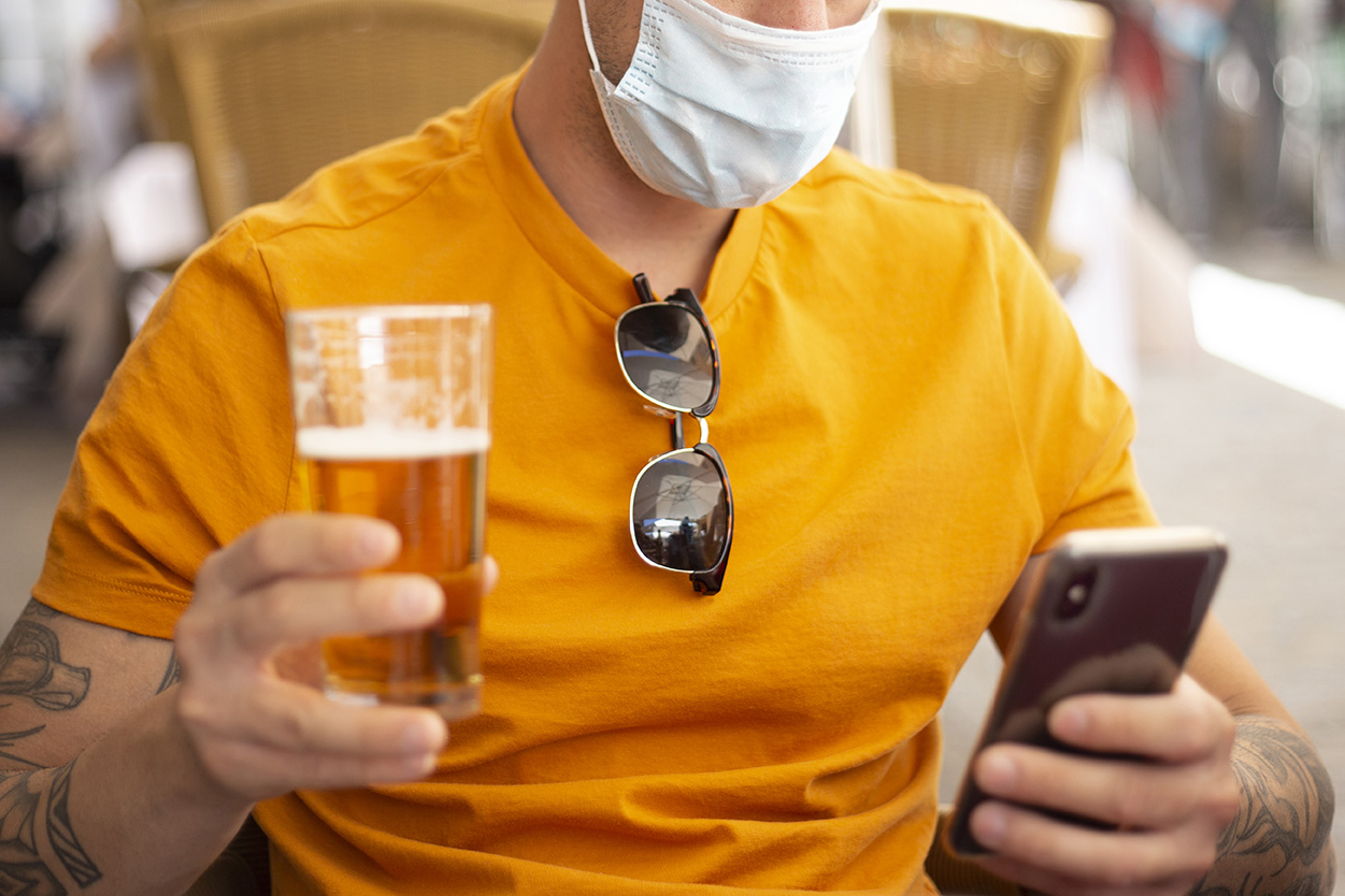 man wearing a mask with beer and phone in hands